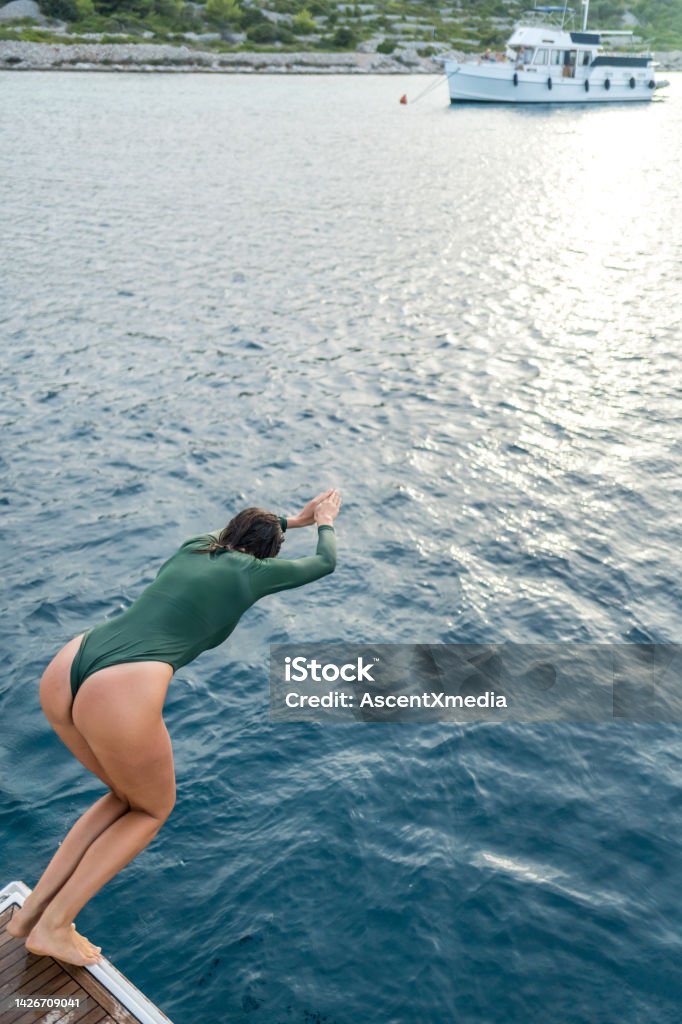 Young woman dives into sea from boat She is wearing one piece bathing suit Water Stock Photo