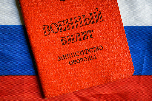Certificate of Russia serviceman on Russian flag on table, top view. Concept of mobilization, war in Ukraine, soldier, duty and army. Translation: Military ID card, Ministry of Defense.