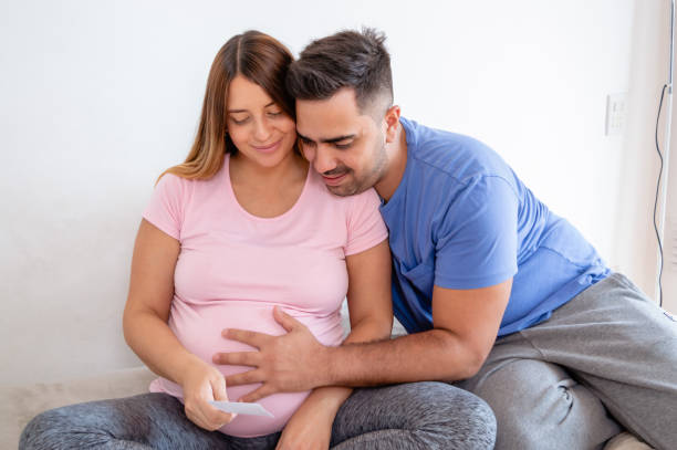 pregnant couple sitting on bed happy looking at printed ultrasound photo stock photo
