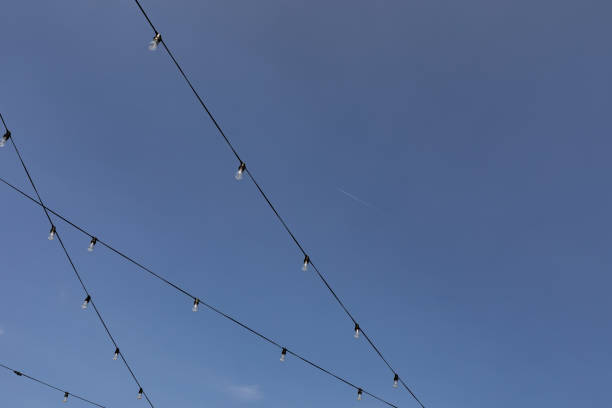 istock Black wires suspended before a blue sky with lightbulbs, creative copy background 1426727957