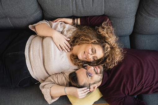 Above shot of a happy mid adult couple lying down on the sofa and enjoying together