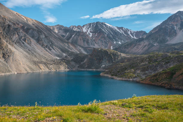 istock Deep mountain lake of phantom blue color among sharp rocks and high mountains in changeable weather. Wonderful dramatic view from sunlit grassy hill to deep blue alpine lake and rocks under cloudy sky 1426729208