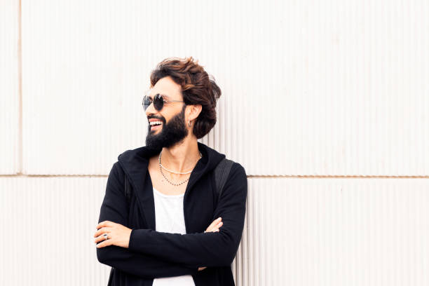 beautiful young man with sunglasses smiling happy leaning in a white wall, concept of urban lifestyle and stylish clothing, copy space for text