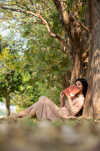 a woman sitting under a big tree reading a book