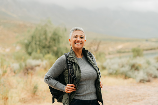 Happy elderly woman and backpack in nature for adventure, happiness and joy in the outdoors. Portrait of a female senior tourist or adventurer smiling on a journey outside with a natural background.