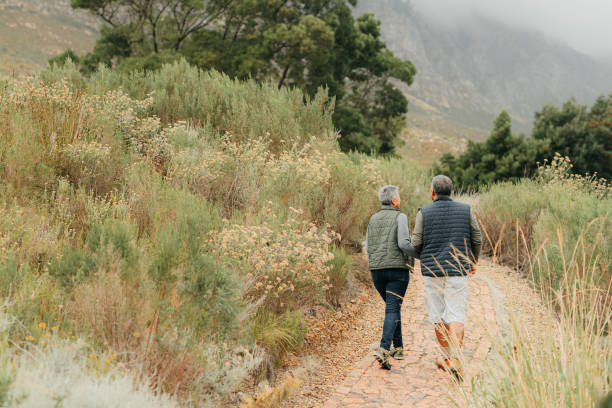 Senior hiking couple in nature trekking by mountains and wild grass together for exercise, walking and wellness outdoors. Friendship, people and woman love relaxing, adventure and healthy retirement stock photo