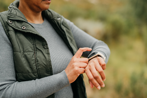 Nature, exercise and hiking woman checking her digital fitness watch while walking on hike trail. Closeup of a fit, active and mature lady with activity tracker wrist band on adventure health workout