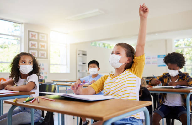 istock Learning, education and classroom in covid pandemic with students wearing face mask for protection against the spread of the virus or diseases. Clean inside school with dedicated and smart children 1426755518