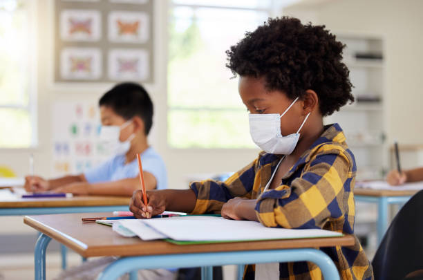 istock School student in class during covid pandemic for learning, education and study with mask for safety, protection and protocol. Little kindergarten, preschool or elementary kid writing in book at desk 1426755539