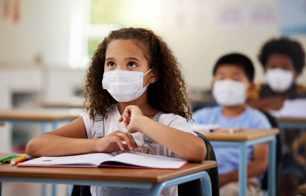 istock School student with covid learning in class, wearing mask to protect from virus and looking concentrated on education in classroom. Little girl sitting at desk, studying and listening during pandemic 1426755566