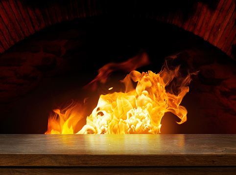Side view of an empty wooden tabletop with open fire oven on a dark background.