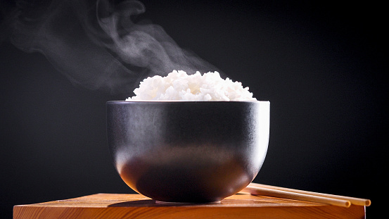 Arroz japonés, Arroz cocido. Close up natural humeante arroz blanco japonés cocido en tazón negro con palillo sobre fondo negro, enfoque suave. Concepto de Comida Saludable. photo