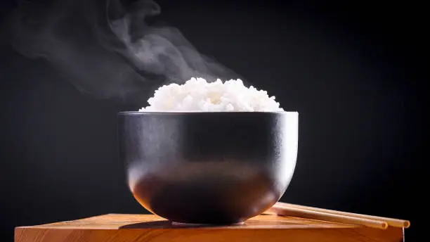 Japanese rice, Cook rice. Close up natural steaming cooked Japanese white rice in black bowl with chopstick on black background, soft focus. Healthy Food Concept.