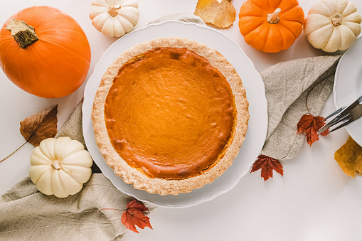 Traditional autumn food, pumpkin pie and colorful pumpkins on the white table, top view