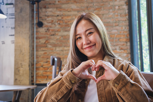A beautiful young asian woman making heart hand sign with feeling happy