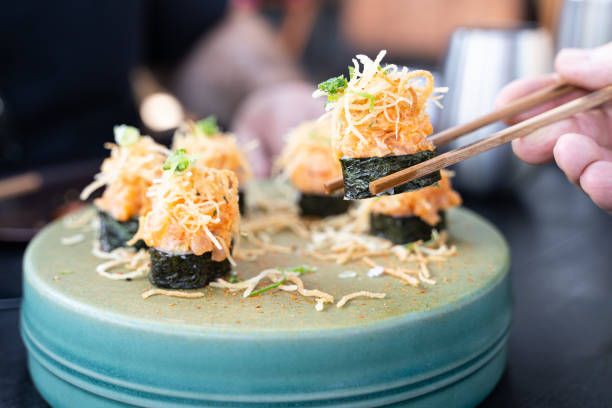 Cut maki salmon sushi rolls, spicy mayo chopsticks holding one piece