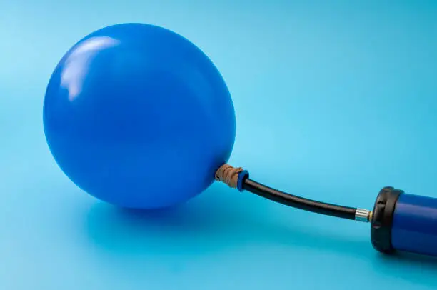 Photo of Party accessory, fun decoration and financial bubble with pump inflating a latex balloon isolated on blue background with copy space on the blank balloon