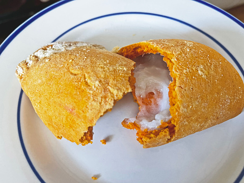 A Guatemalan empanada with Manjar (Empanada de Manjar).   Broken in two to show the white manjar inside.   Yellow empanada (empanada amarilla).    On a white plate with blue trim.
