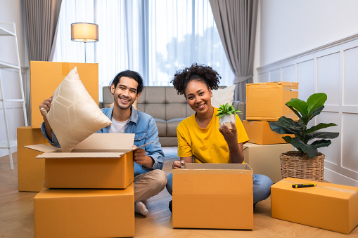 Young  couple man and woman looking satisfied sitting on the floor hugging during moving to new apartment unpacking boxes.