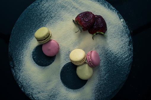 Assorted flavoured macaroons on a black slate board with strawberries