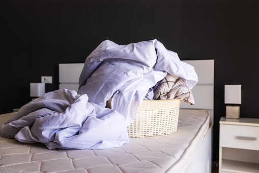 A large pile of dirty linen on the bed is collected in a basin to be washed. The concept of homework, cleaning in the apartment, studio, apartment booking. Laundry concept, liquid bed linen detergent