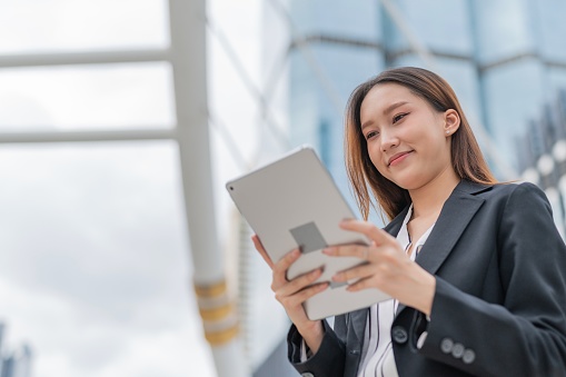 Portrait moment photo of an attractive young asian professional businesswoman lady with nice smile on her face looking at latest update of the marketing and sales inventory report on her digital tablet in a central business district in Bangkok city