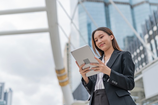 Portrait moment photo of an attractive young asian professional businesswoman lady with nice smile on her face looking at latest update of the marketing and sales inventory report on her digital tablet in a central business district in Bangkok city