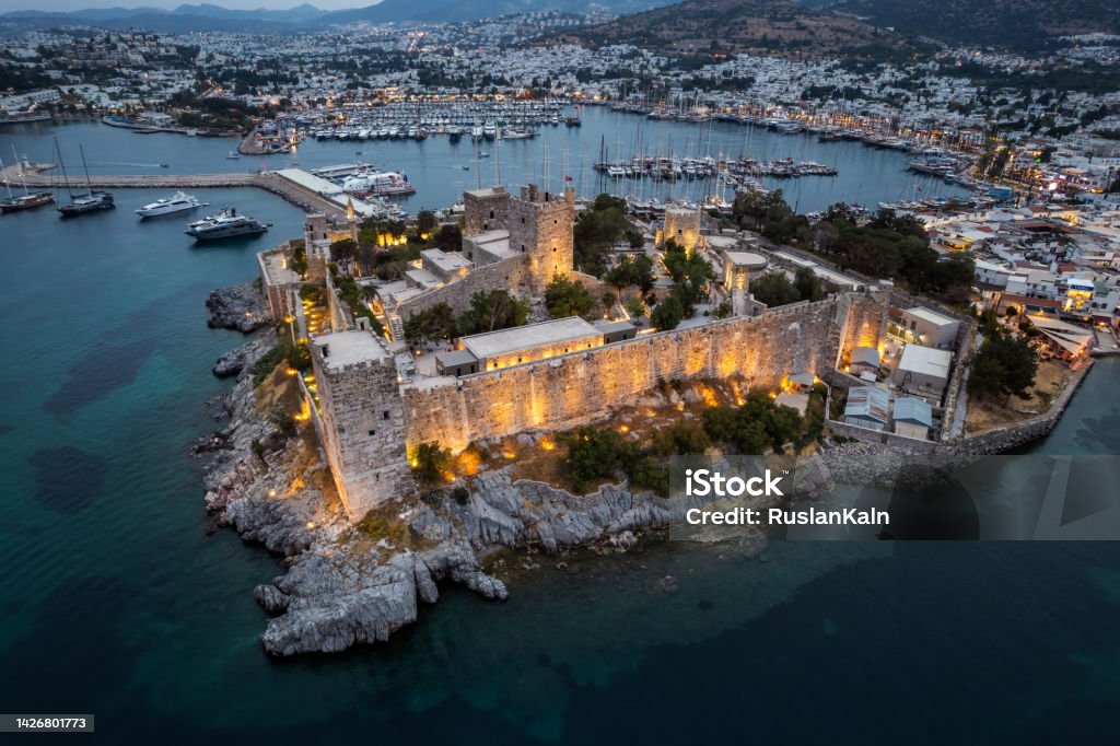 Main tourist attractions of Turkey Bodrum bay and ancient castle of Saint Peter at the sunset. Boats floating on calm blue sea. Mountains in the background. Aerial view from drone. Bodrum Stock Photo