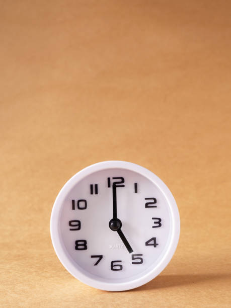 istock Close up, white clock shows time at 5 o'clock on the office brown workplace tabletop. 1426808014