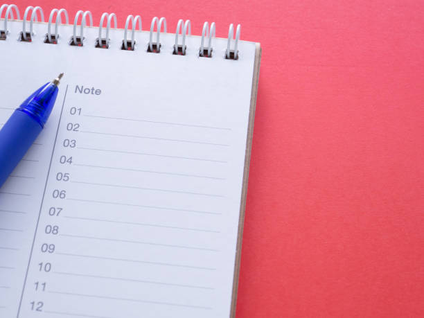 istock Notepad with numbers 01-12 and blue pen on a red workplace offiec background. Blank notebook with text note. Reminder concept. 1426808158