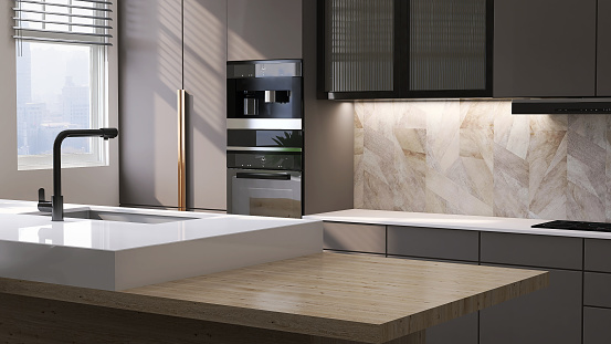 Modern and luxury built-in gray wooden kitchen counter with white laminate top, cabinet, oven and wooden top island with sink and marble tile wall in sunlight from window for product display