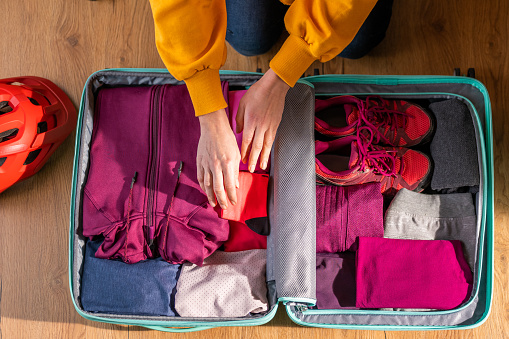 Woman packing hiking clothes in suitcase, high angle view, trekking adventure preparation. Folded pink sport suit in open luggage, vacation on nature planning