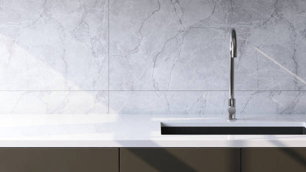 istock Modern and minimal built-in gray kitchen counter with white laminate top, sink and white marble tile wall in sunlight from window 1426824543
