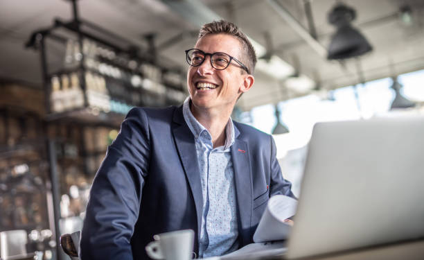 Entrepreneur smiles at the computer screen while having a coffee during a business break in a vintage restaurant.