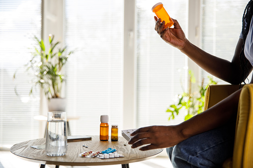 Copy space shot of unrecognizable young woman sitting at her coffee table, holding a pill box and reading the label when organizing her meds for the week.