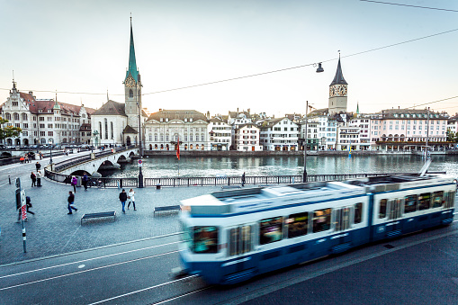 Zurich, Switzerland - October 5, 2016: People are crossing the Helmhaus bridge over the Limmat river leading to Fraumunster as the blue tram arrives at the Helmhaus station. Long exposure.