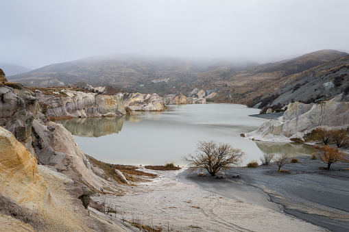 Blue lake at St Bathans with fog drifting over the hills in winter, Central Otago.
