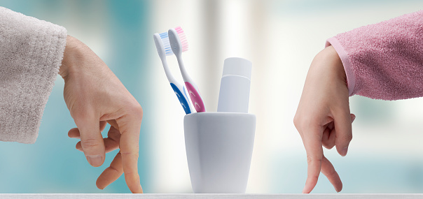 Man and woman in bathrobe walking fingers towards their toothbrushes and toothpaste