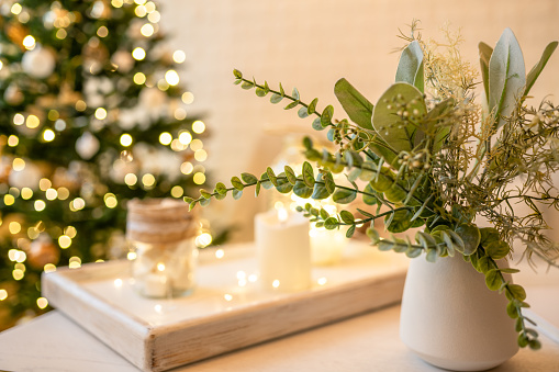Christmas decoration with tray, candle, garland lights, christmas tree and eucalyptus branches in a vase on the table