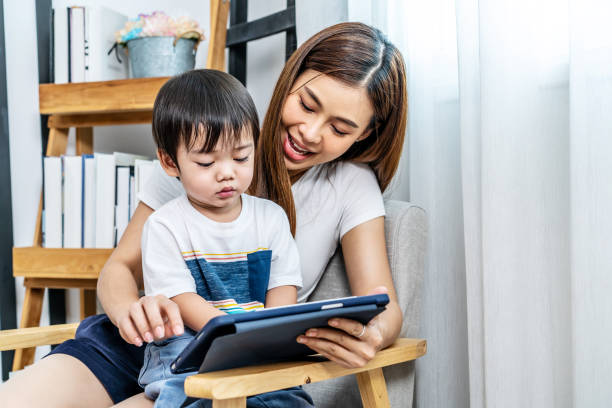 istock Young asian mother her little adorable son using tablet looking at  screen enjoying watching funny social media video doing online shopping relaxing on sofa at home together 1426851033