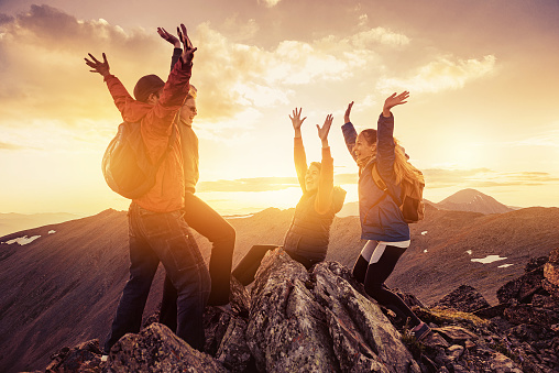 Four happy hikers celebrating climbing on mountain top at sunset