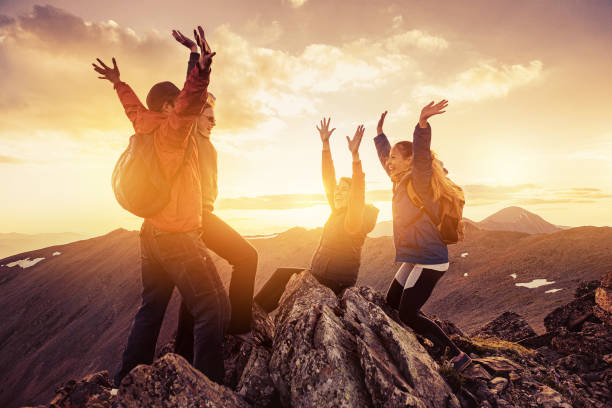 Four happy hikers on mountain top at sunset stock photo