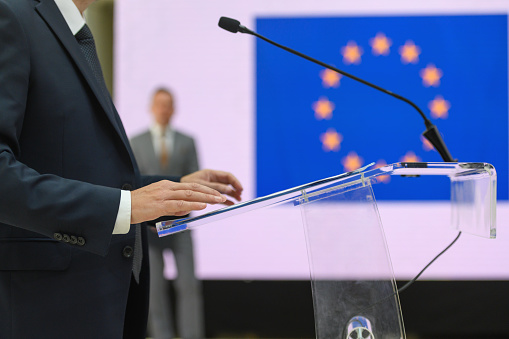 Smiling Muslim politician in ghutrah and agal standing at rostrum podium and speaking in public using mucrophone at international conference