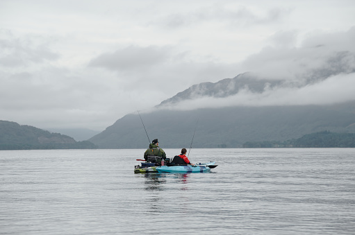 Fishing from kayak on calm water surrounded by mountain scenery Scotland UK