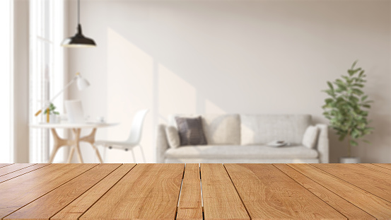 Mesa o encimera de madera en moderna y lujosa sala de estar blanca con pared blanca, escritorio, sofá y planta de interior con luz solar en casa photo
