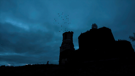 Mystical silhouette of a temple or castle against the cloudy sky and ravens flying in the sky at night. Video. The big old stone Castle on the Rock during the heavy storm and rain. Ancient frightening church in twilight