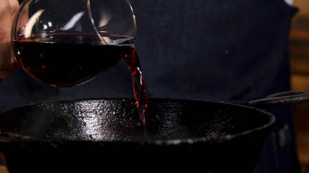 verser le vin rouge dans la poêle. images d’archives. gros plan des mains masculines du chef ajoutant du vin rouge dans une poêle en fer noir pour cuire une sauce spéciale. - black olive photos et images de collection