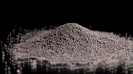 Close up of black pepper pile lying on the black surface and on a black background, cooking food and spices concept. Black pepper corns, small grains.
