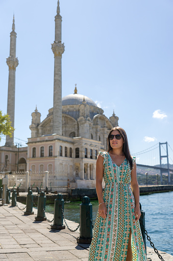 Young woman wearing glasses and dress at Ortakoy Mosque with Bosphorus Bridge in Istanbul.