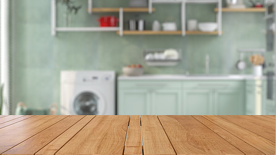 Wooden tabletop or countertop in laundry utility room with green counter, shelf and white washing machine, basket and green wall with sunlight at home for household washing and cleaning product display